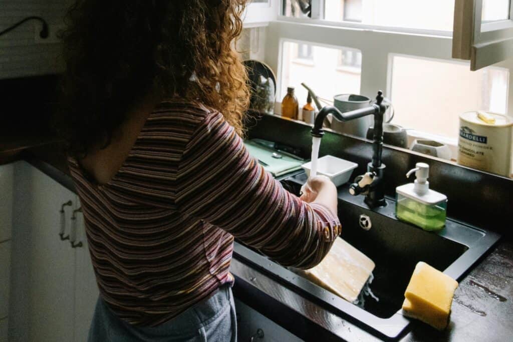 A young woman washing a chopping board by the sink through running water in the concept of "changing address and updating utilities after moving to Wandsworth'.