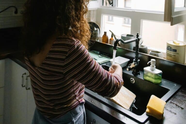 A young woman washing a chopping board by the sink through running water in the concept of "changing address and updating utilities after moving to Wandsworth'.