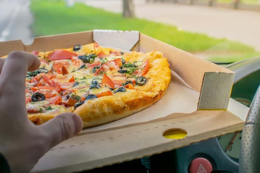 Cropped image of a man's hand reaching for a pizza slice while en route to his new house